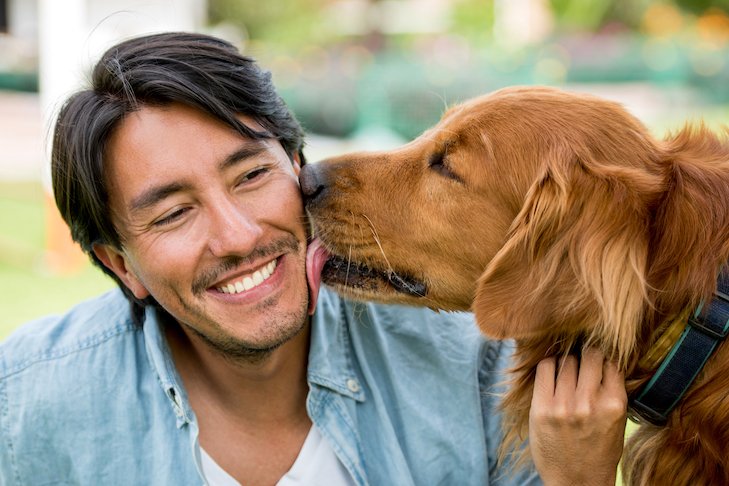 Portrait of a beautiful dog licking a happy man smiling outdoors